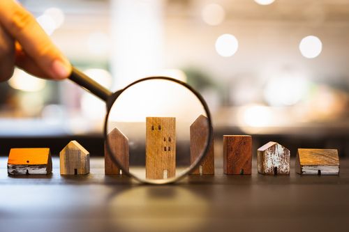 Lupe vergrößert Miniaturhochhaus aus Holz